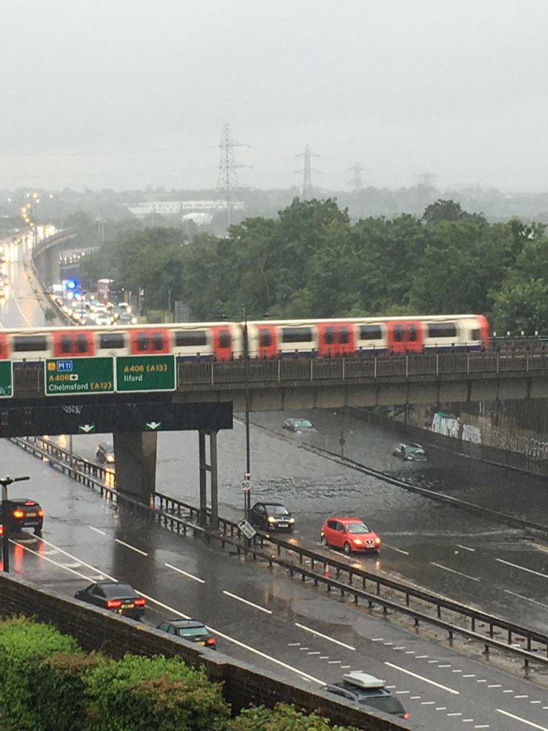 Flooding causing traffic issues in East London, UK with tube train passing overhead.